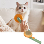 Cat being groomed with a pet brush featuring a pumpkin design, held by a person.