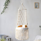 Hanging macrame chair with a cat inside against a light gray wall.