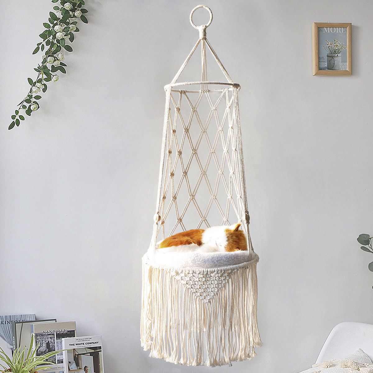 Hanging macrame chair with a cat inside against a light gray wall.