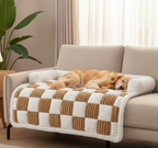 Dog lying on a checkered blanket on a couch in a living room.