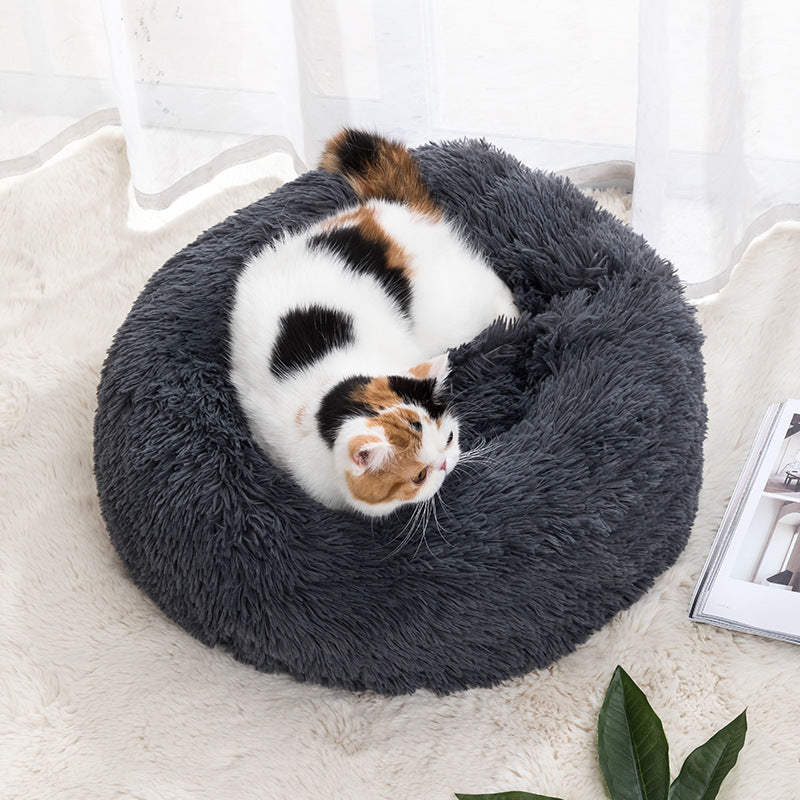 A pet bed in a round shape with a brown color, where a white cat is resting inside.