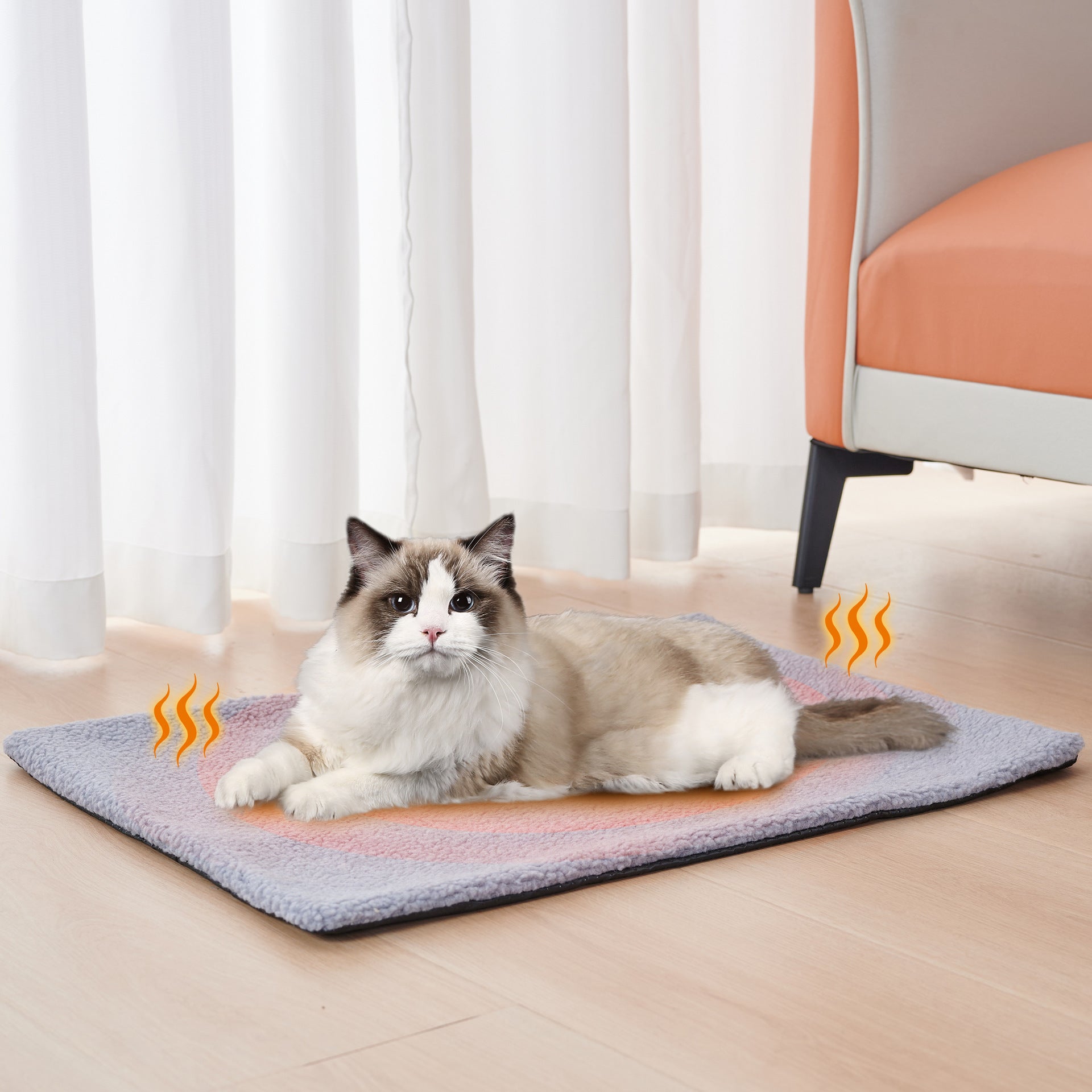 Cat lying on a heating pad in a room with white curtains and an orange chair.